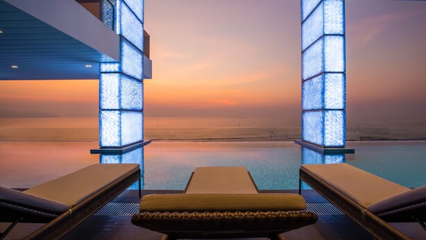 A poolside lounge area with a view of the sea at sunset. - Prince Hotel Da Nang  (Da Nang)