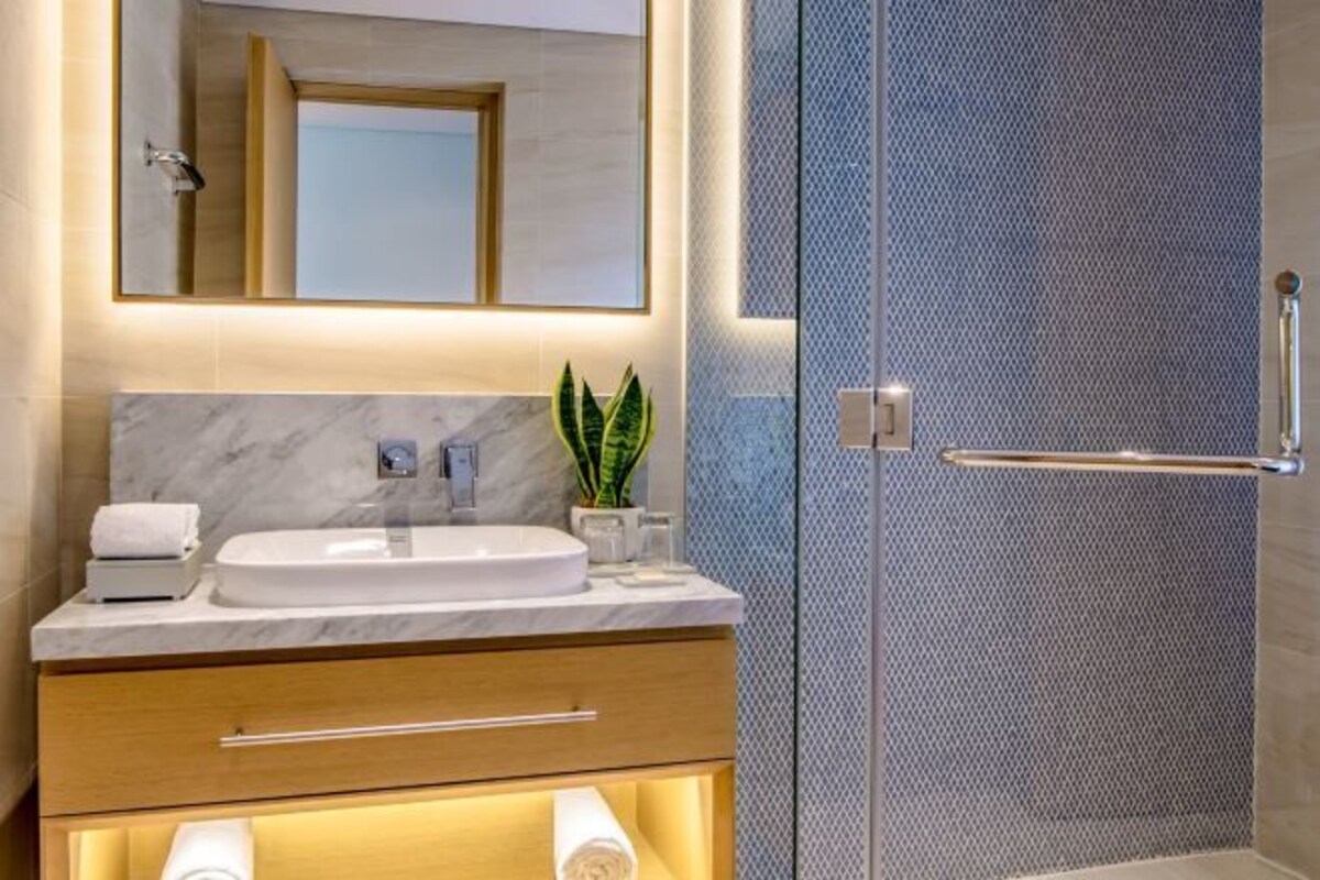 A modern bathroom with a marble sink, a mirror, a towel warmer, and a shower enclosure.