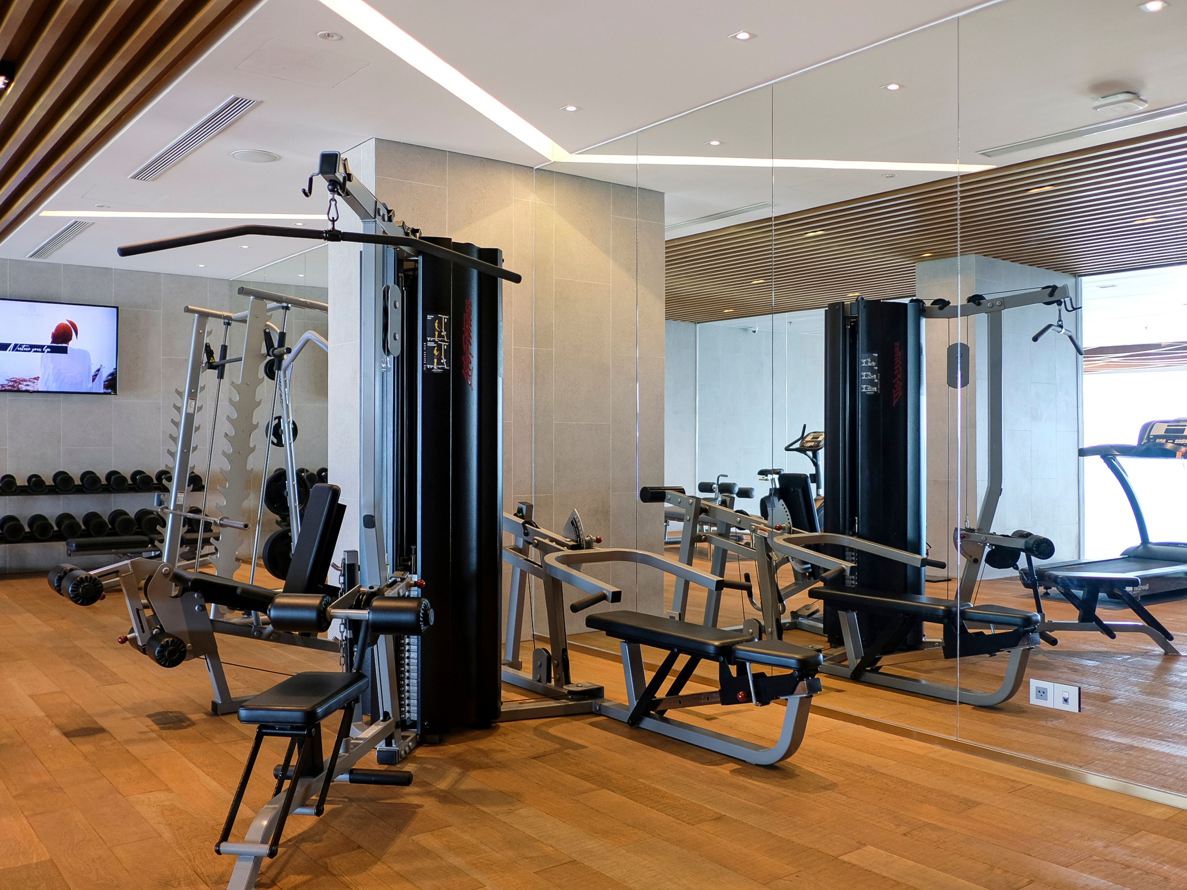 A modern gym with various exercise equipment, a television screen, and a wooden floor.