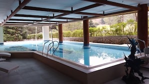 Una piscina interior con vistas al paisaje circundante, sostenida por columnas, y una estatua a la derecha.