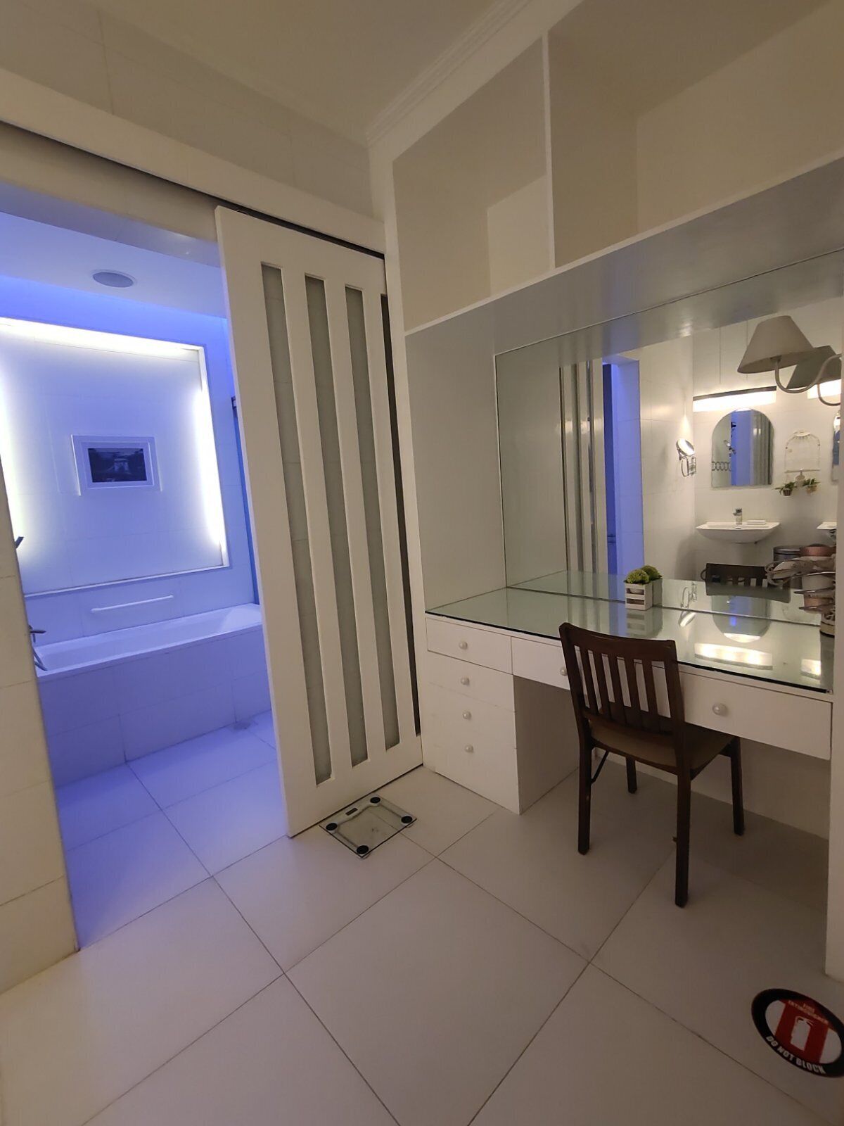 A modern bathroom with a glass vanity, a large mirror, and a shower area with a blue light.