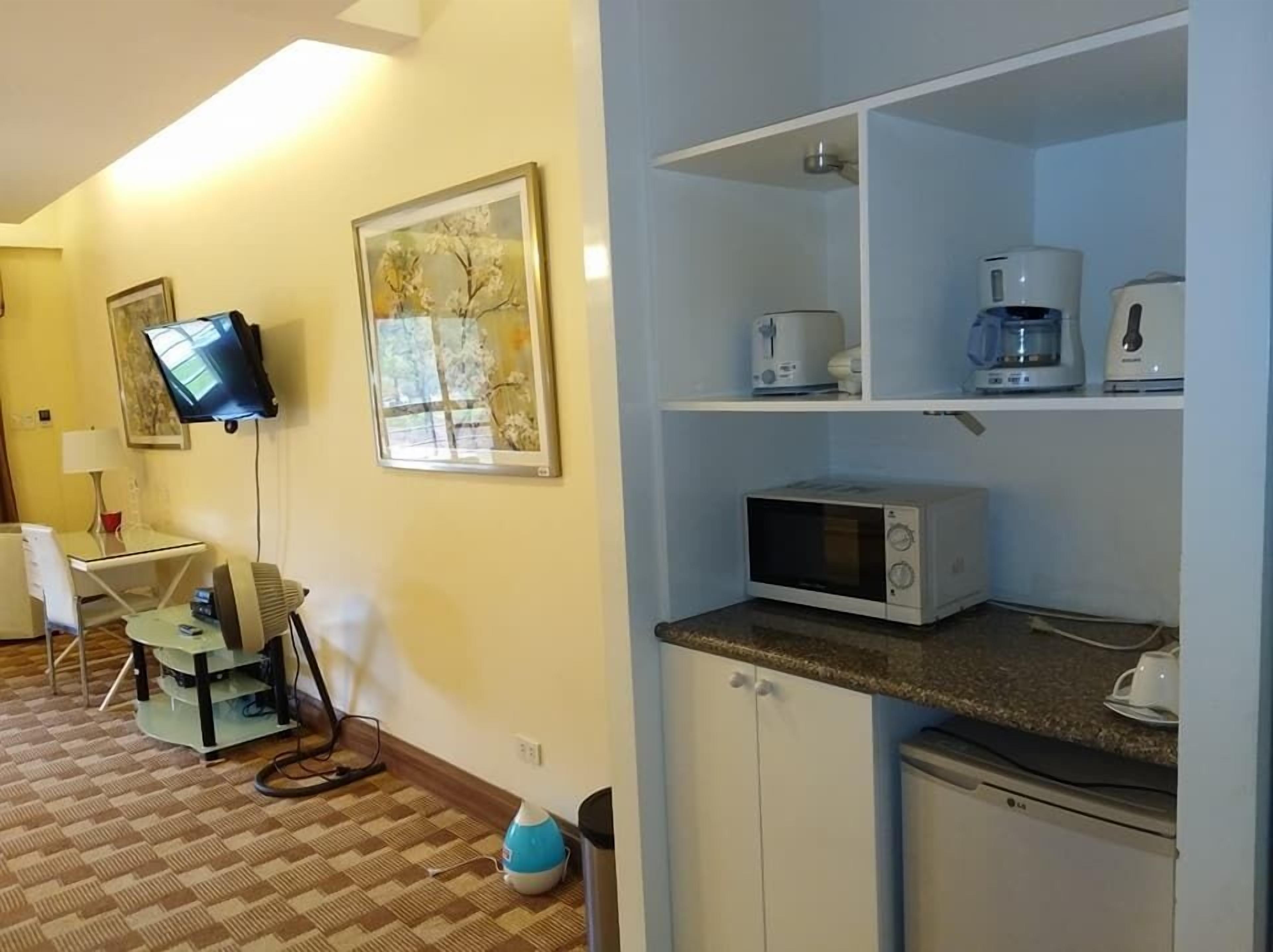 A compact hotel room with a kitchenette, a flat-screen TV mounted on the wall, and a small seating area with a table and chairs.