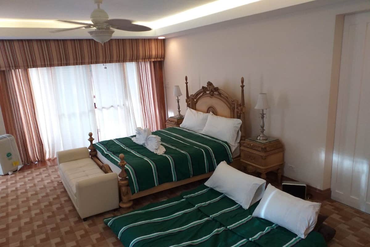 A hotel room with a large bed, a smaller bed, a chair, and a ceiling fan.