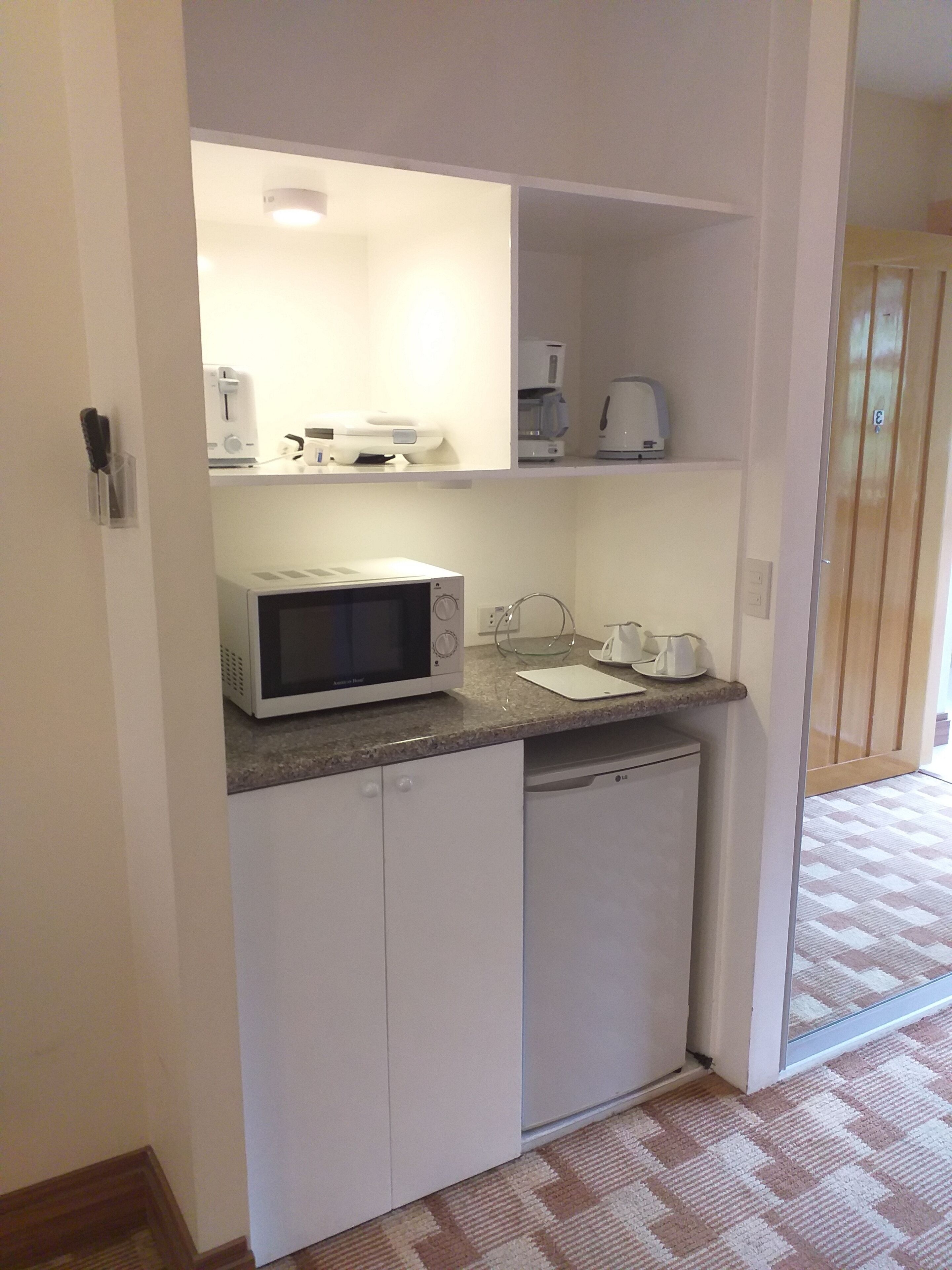 Una kitchenette compacta equipada con microondas, cafetera y una pequeña encimera.