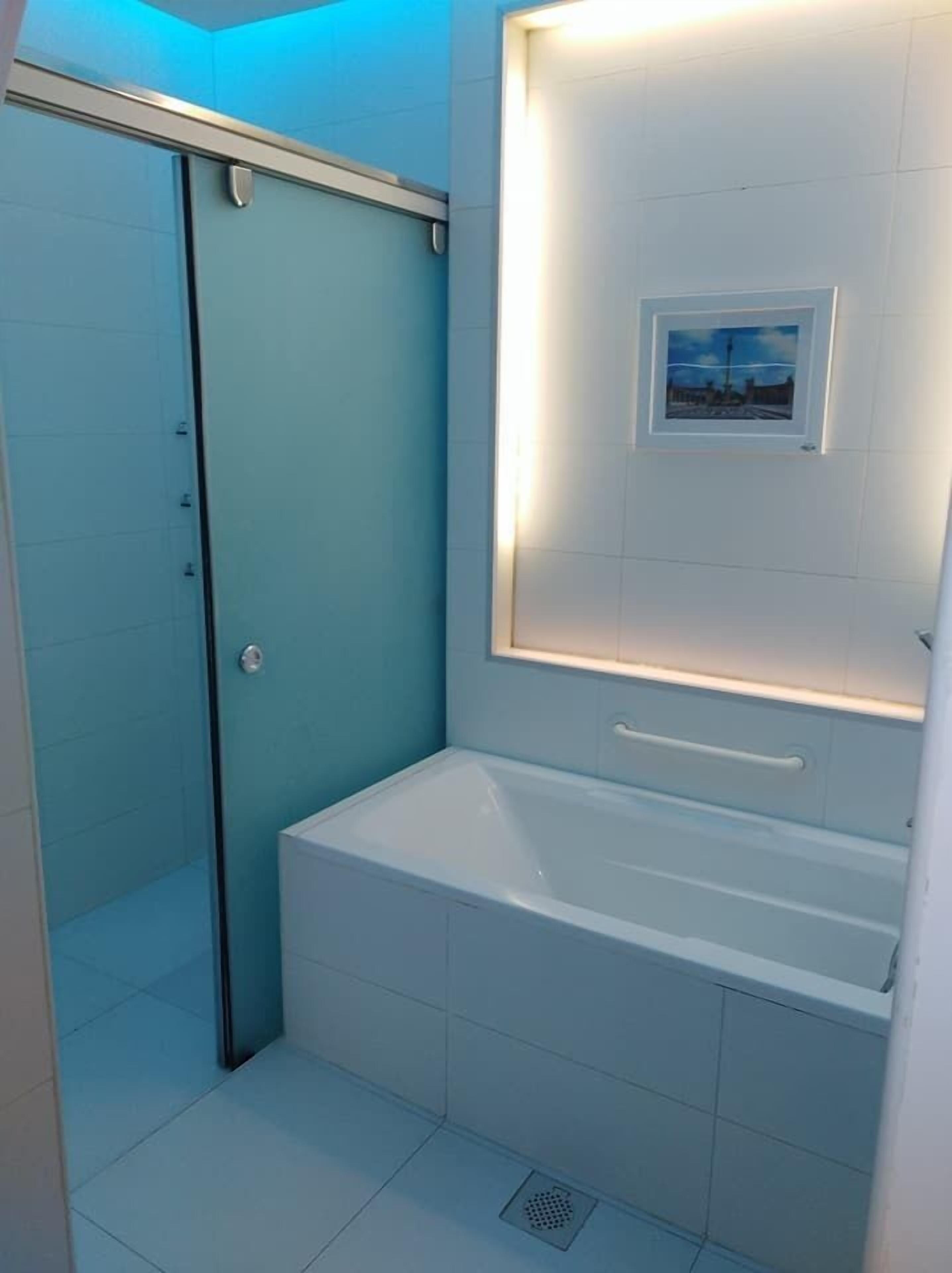 Un baño moderno con cabina de ducha de vidrio, una bañera blanca y un cuadro enmarcado en la pared.