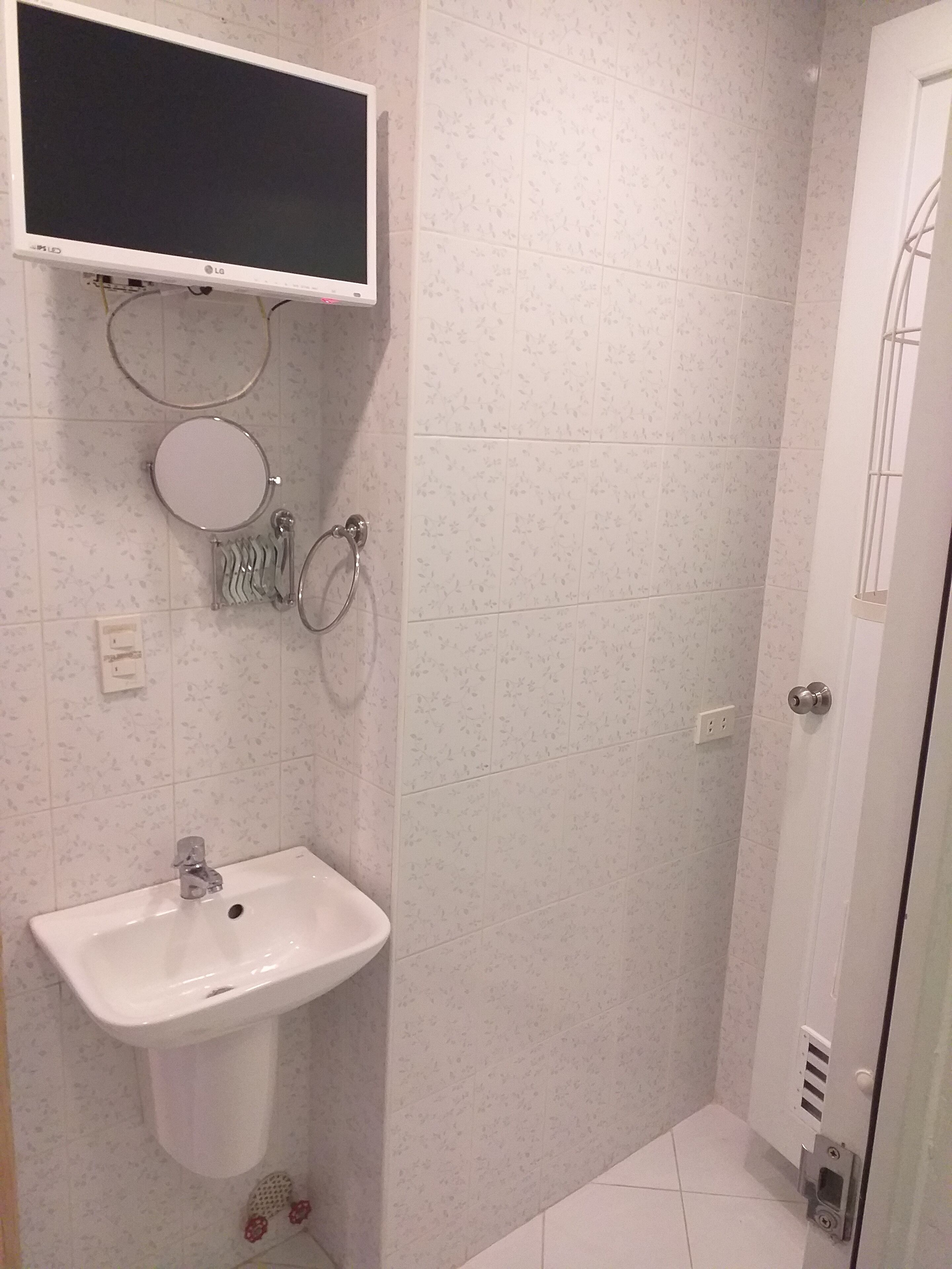 A bathroom with a white sink, mirror, and toilet. There is a shower area with a glass door and a toilet paper holder.