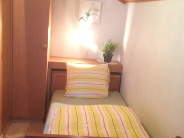 Ein kleiner, gemütlicher Raum mit einem Bett, einem Nachttisch, einer Lampe und einem Topf mit Pflanze.