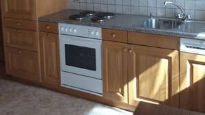 A kitchen with wooden cabinets, a white stove, and a tiled backsplash. - Miranda by Interhome (Saas-Almagell)