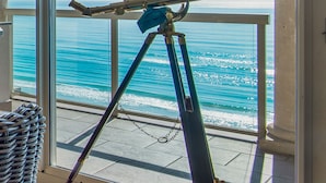 A telescope on a balcony with a view of the ocean.