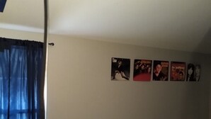 Een kamer met een raam voorzien van blauwe gordijnen, een muur met verschillende posters en een vloerbedekking.