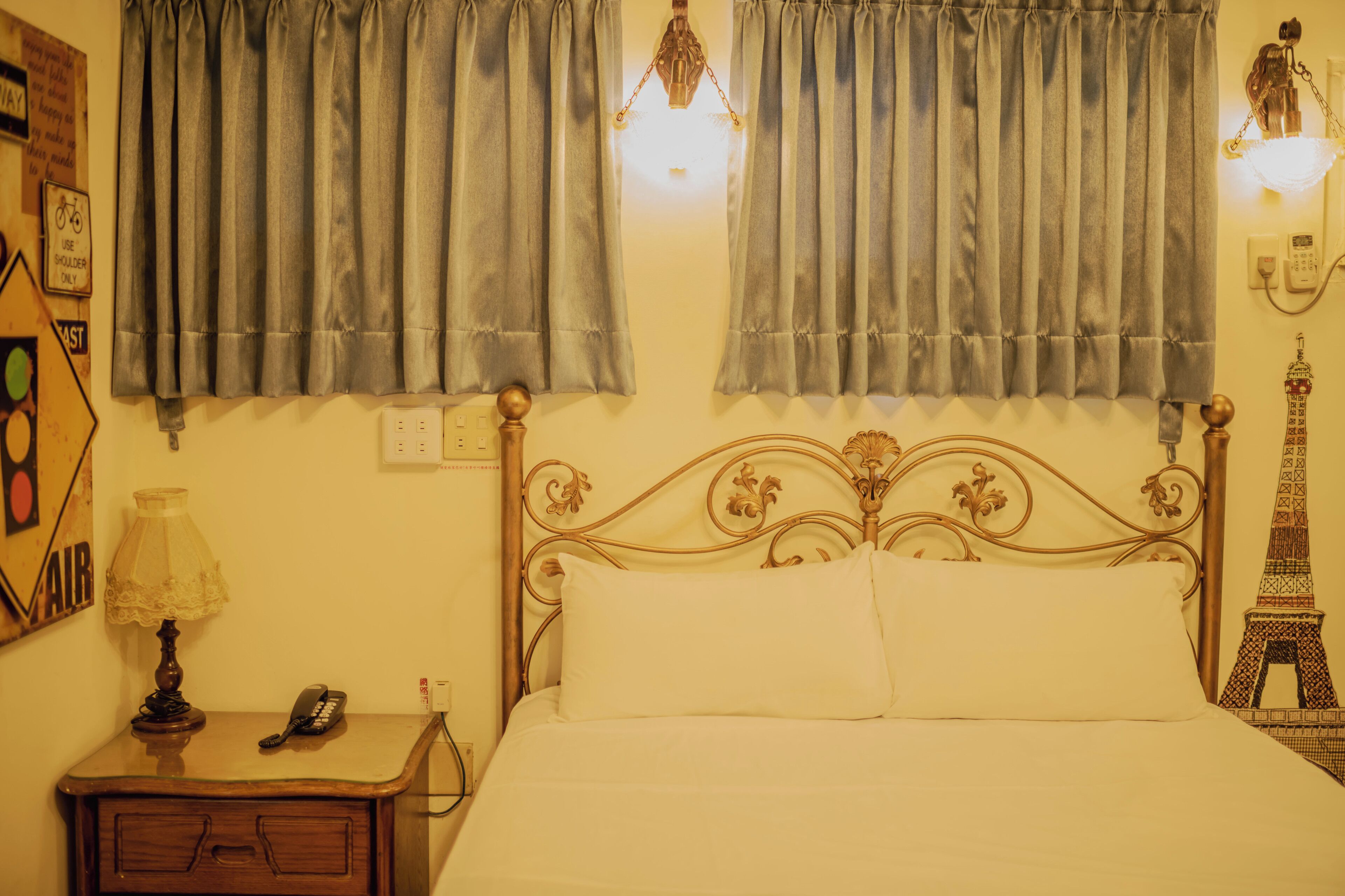 A bed with a metal headboard, a nightstand with a lamp, and a wall-mounted telephone.