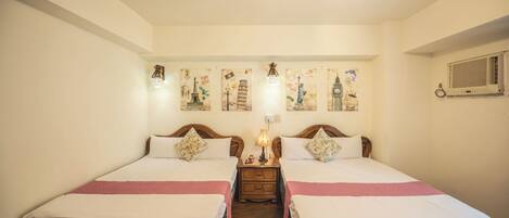 A hotel room with two beds, a nightstand with a lamp, and wall art depicting famous landmarks.