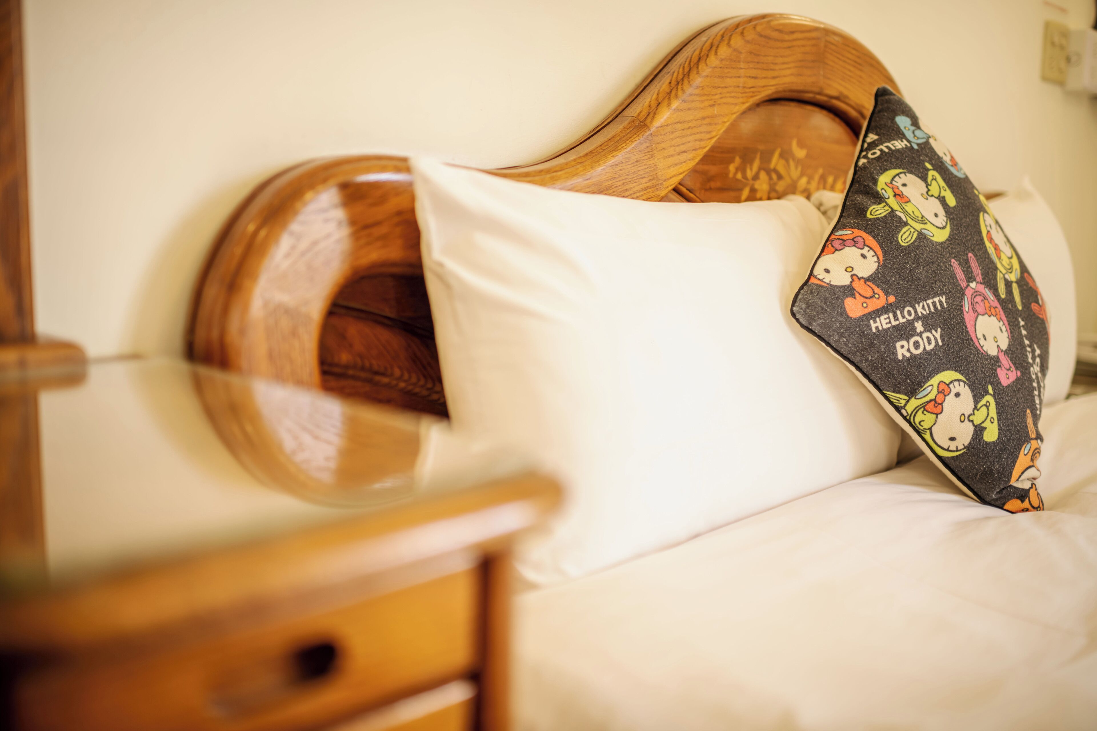 A bed with a wooden headboard, white bedding, and a Hello Kitty pillow.