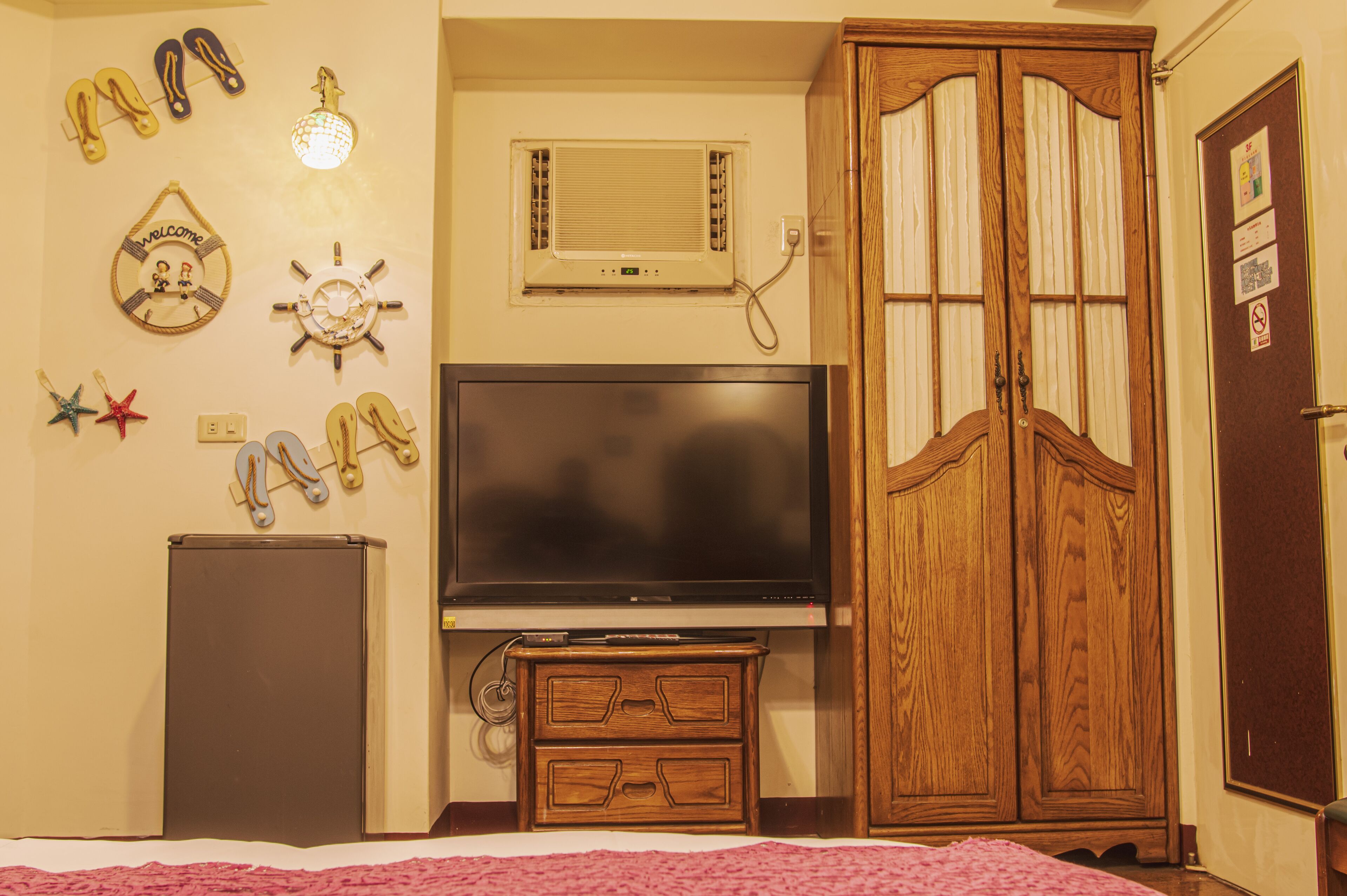 A bedroom with a TV, wooden wardrobe, and wall decorations including a starfish and flip-flops.