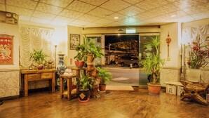 Een hotel lobby met houten vloer, planten in potten, een receptiebalie en een auto buiten.