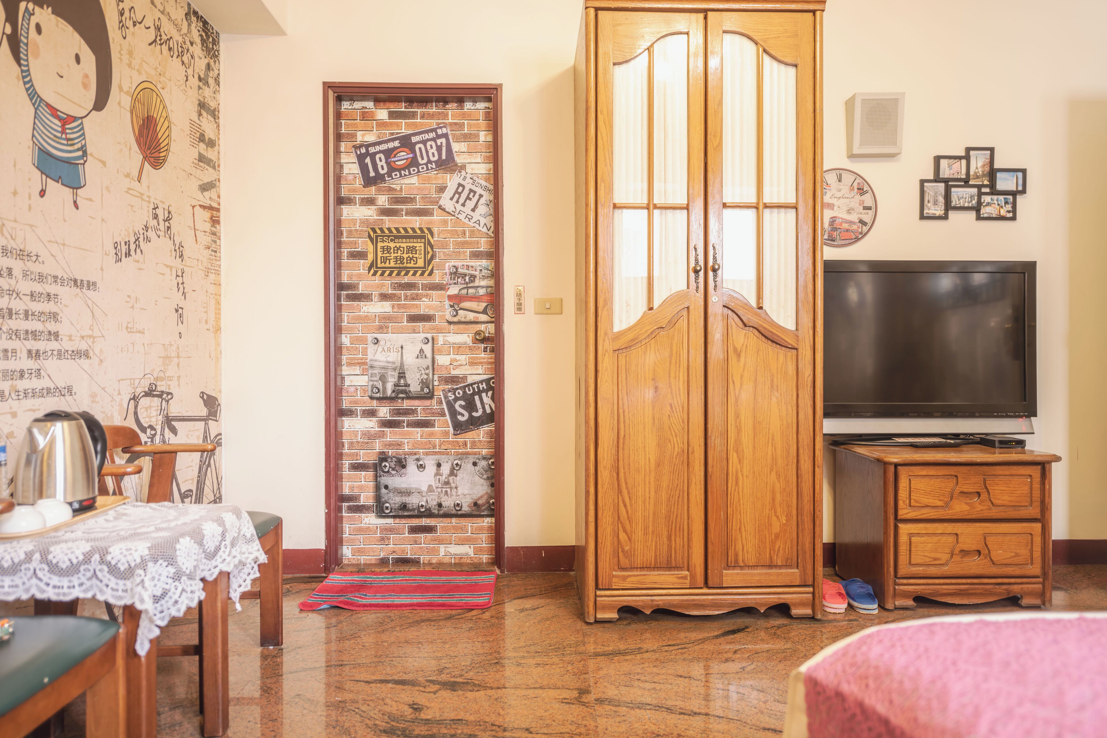 A room with a wooden wardrobe, a television, and a dining table with a lace tablecloth.