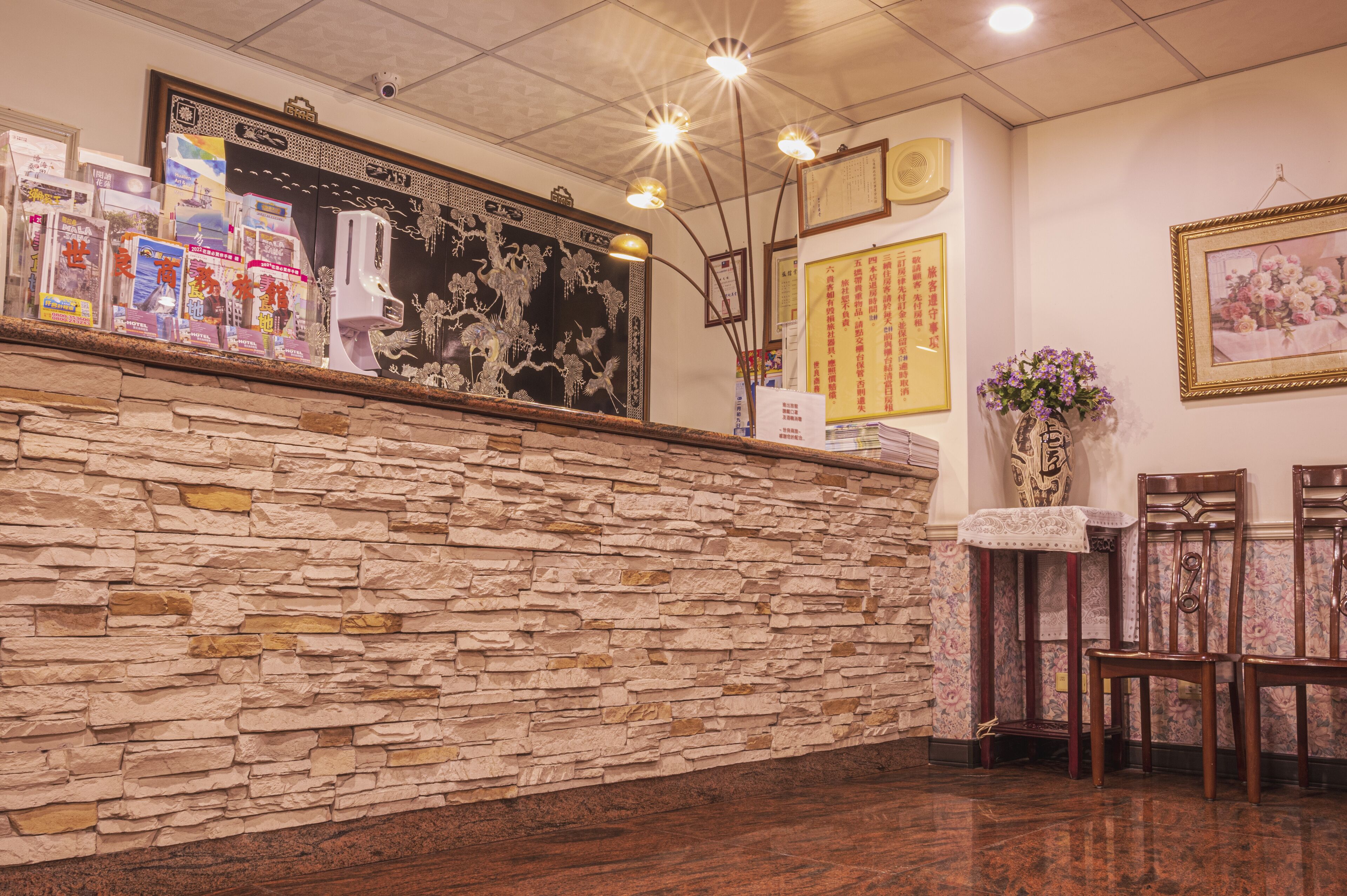 A reception area with a stone wall, a display of books, a framed artwork, and a vase with flowers.