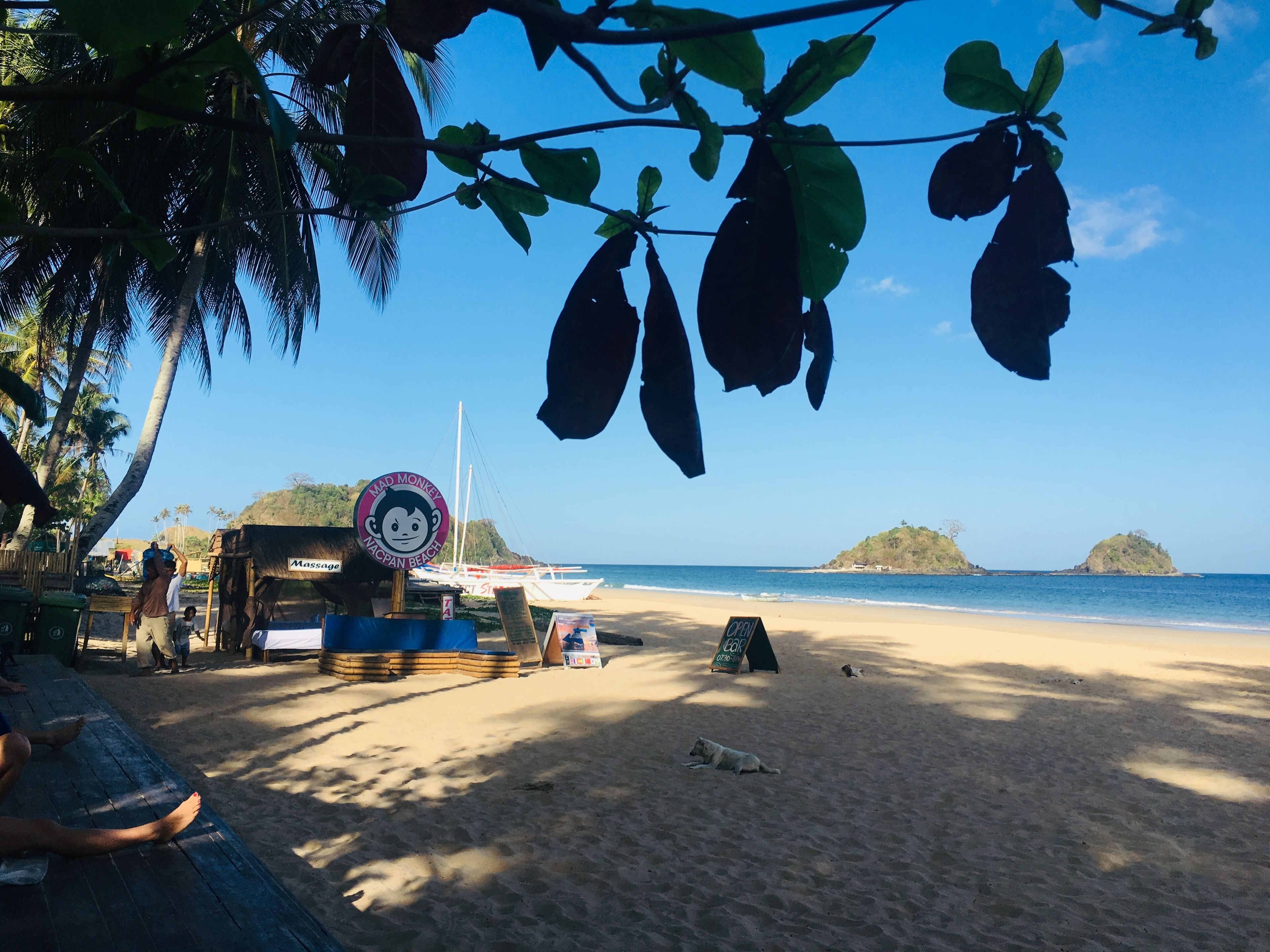 Una spiaggia con un cartello che indica 'Mad Monkey Macapaan Beach' e una piccola kiosk.