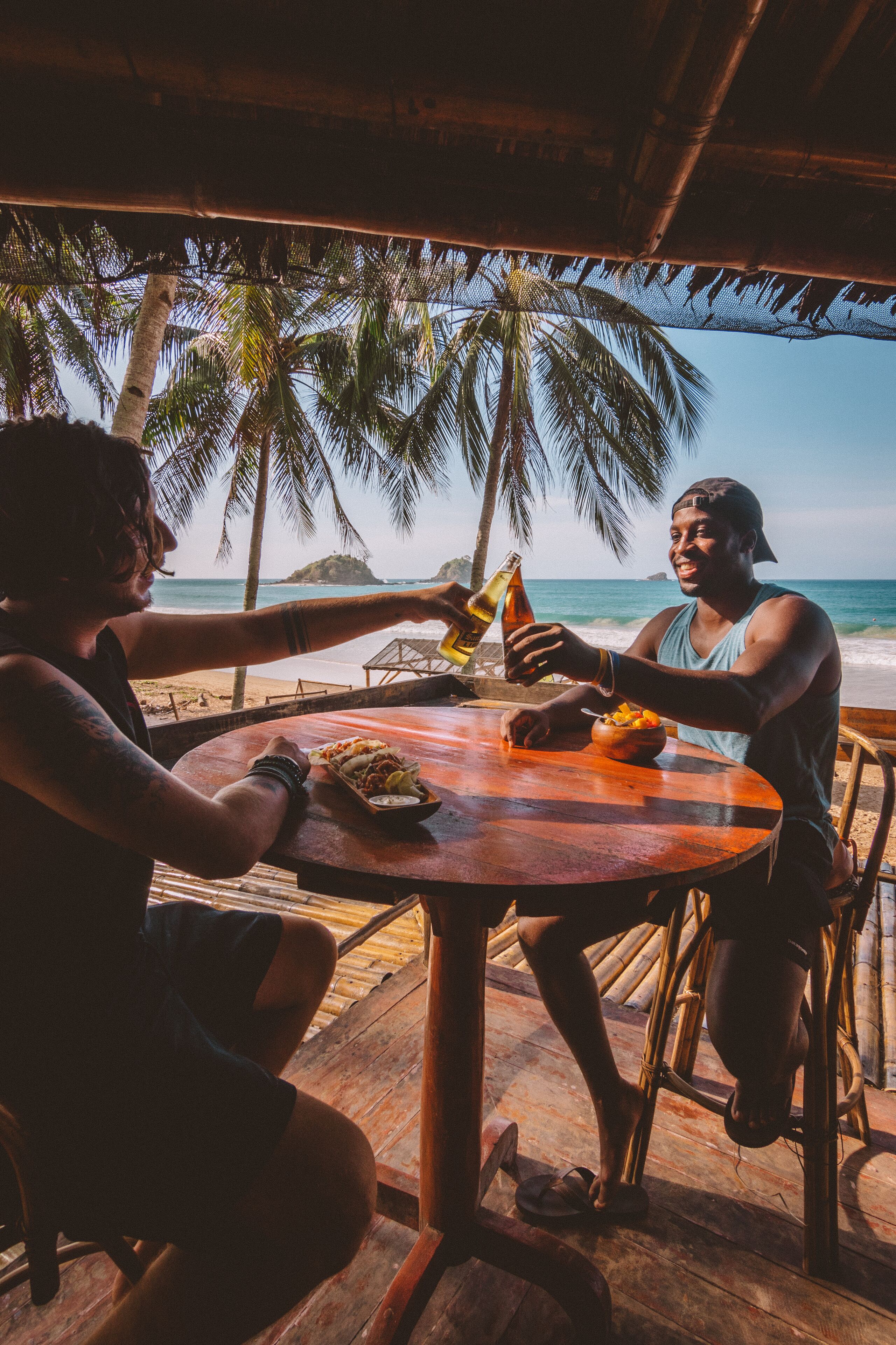 Two people sitting at a wooden table with a view of the ocean and palm trees.