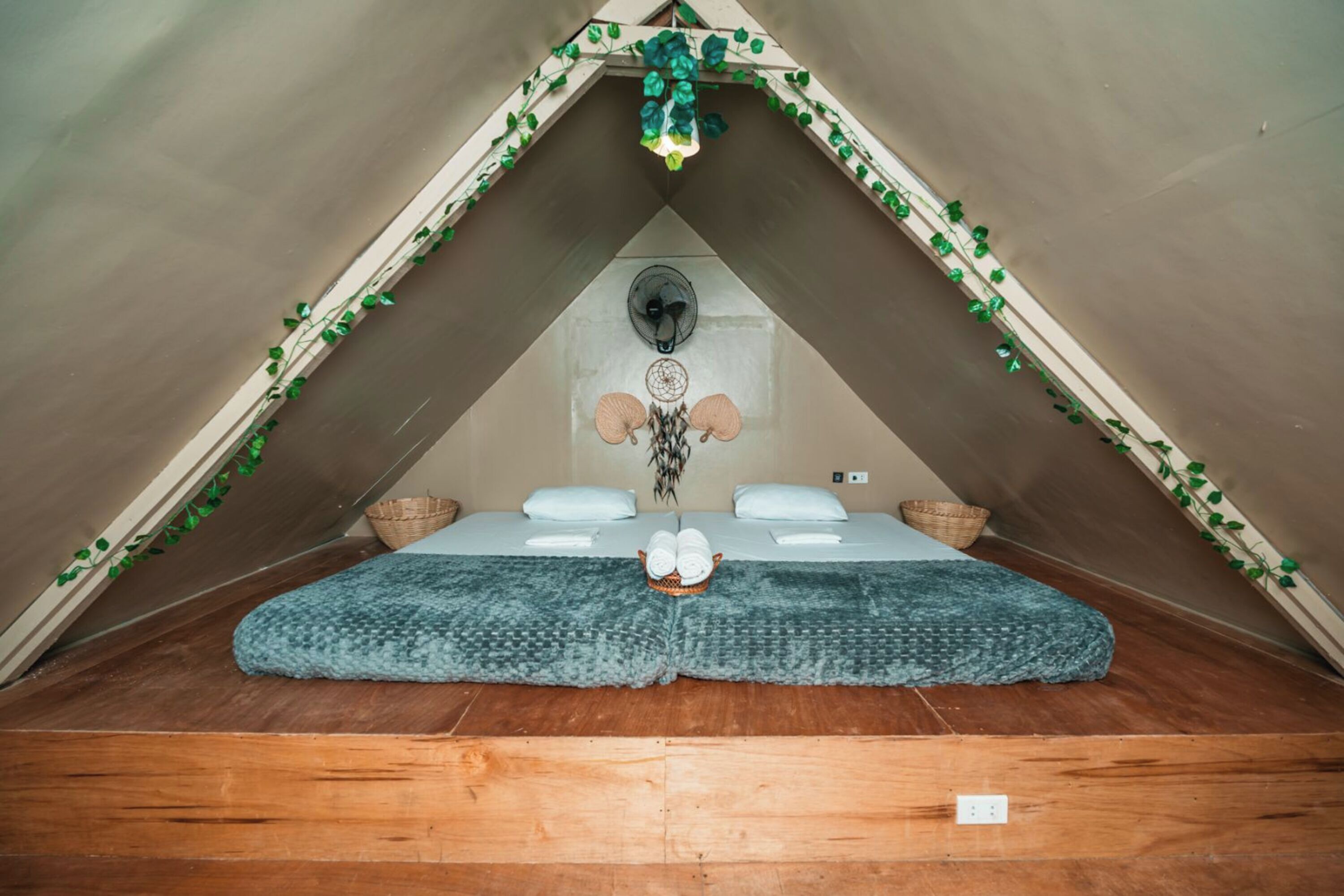 A small, triangular attic room with a bed, pillows, a basket, and a dreamcatcher.