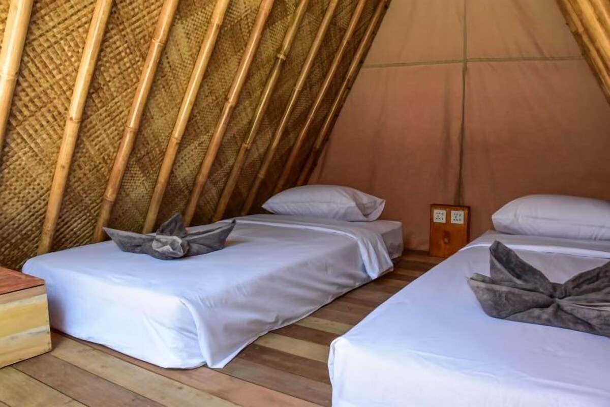 A small, enclosed tent with two beds, each with pillows and a wooden side table.
