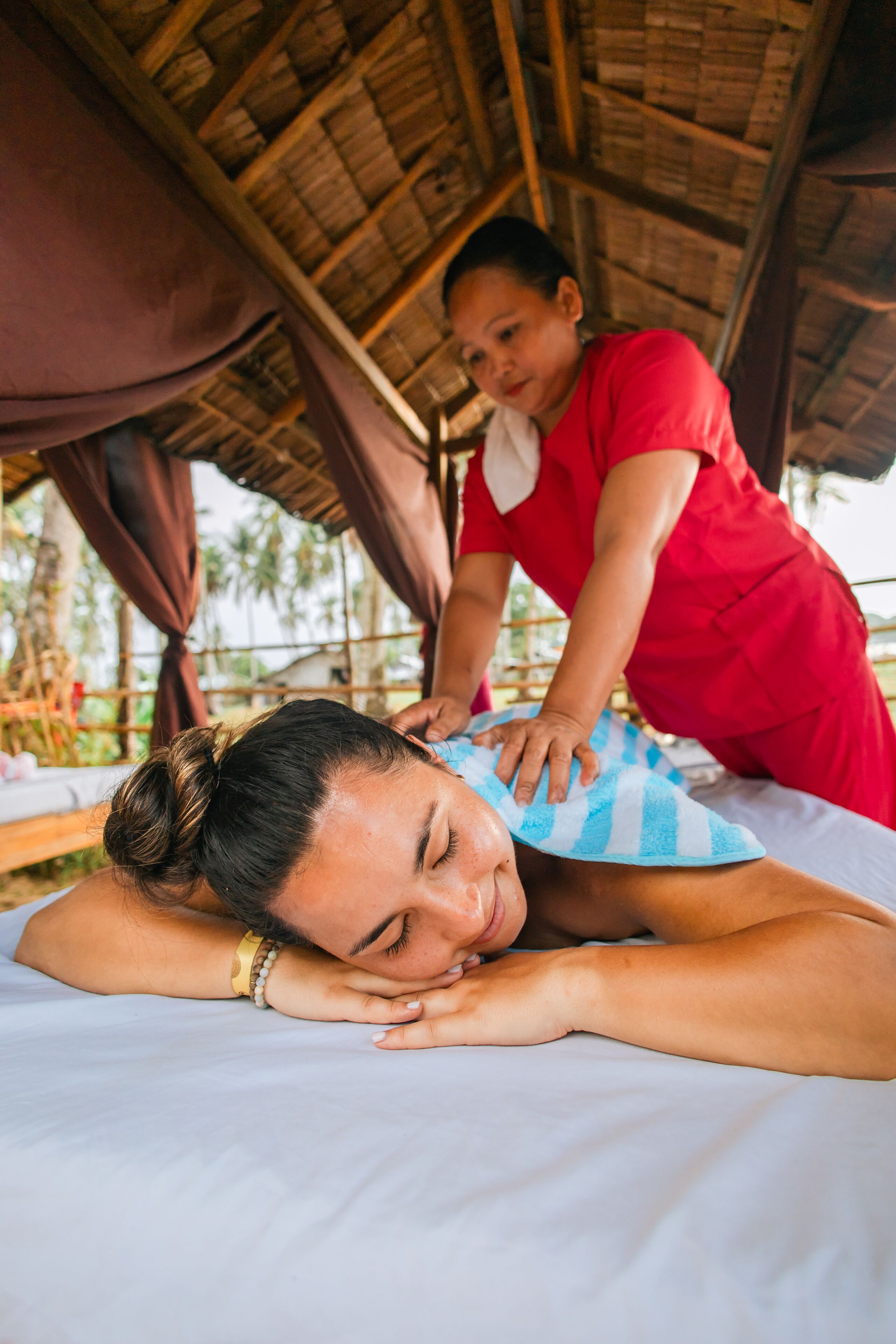 A massage therapy session in a rustic setting with a thatched roof and wooden beams.