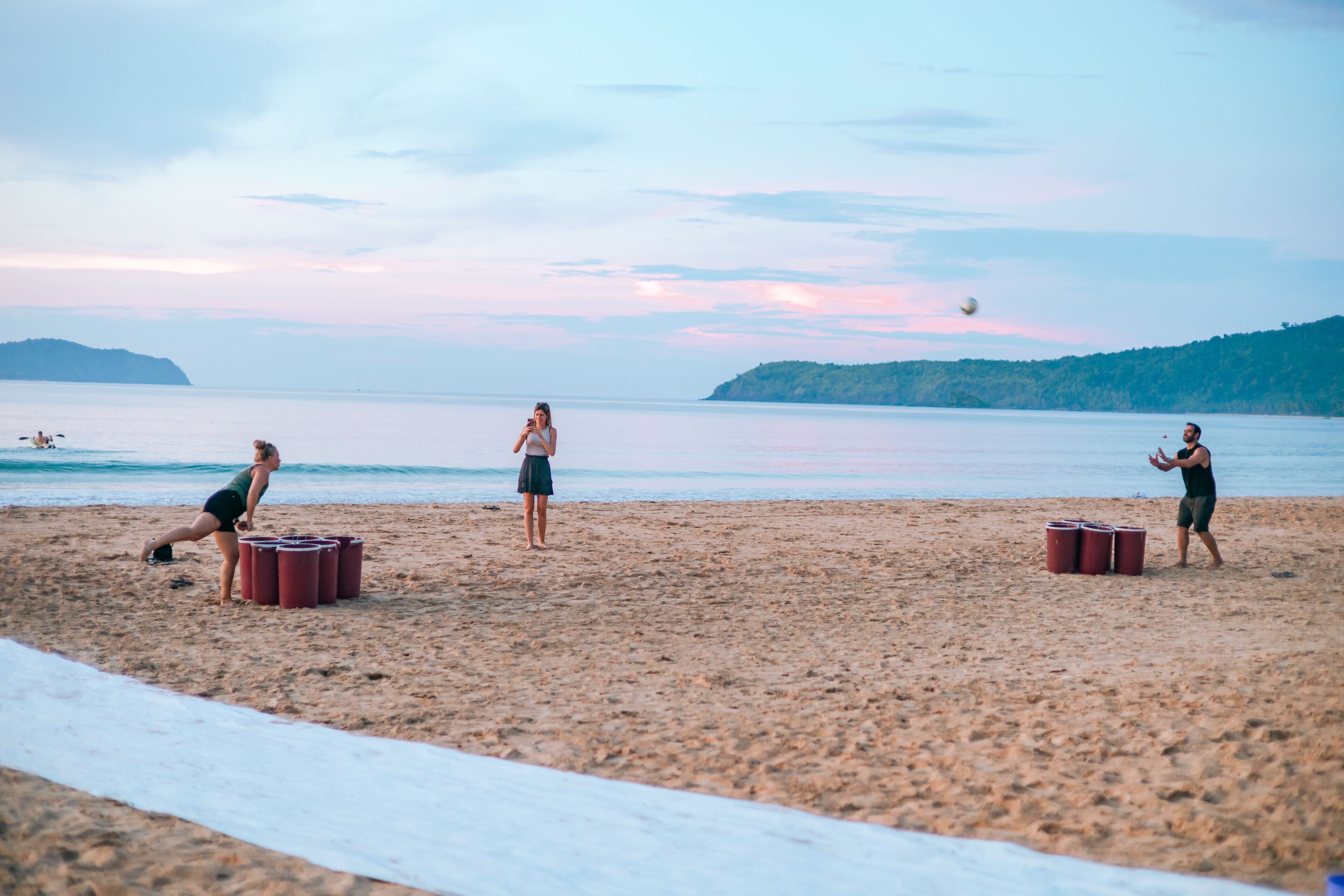 A beach with people playing with buckets, a clear sky, and calm water.