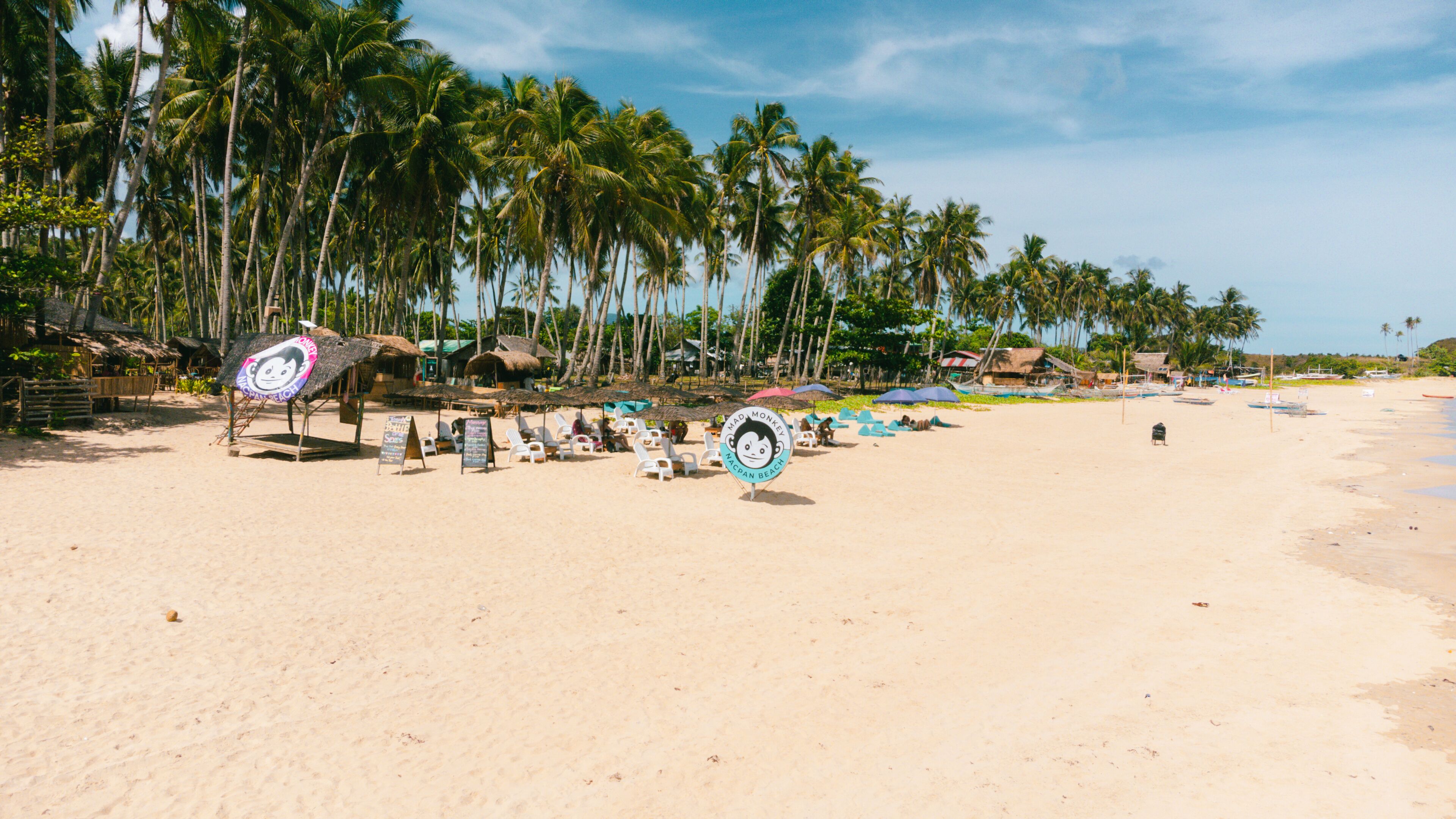 A beach with thatched-roof huts, white lounge chairs, and umbrellas.