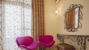 Ein Zimmer mit zwei leuchtend pinkfarbenen Sesseln, einem kleinen Holzschemel, einem dekorativen Spiegel und einer Wandleuchte.