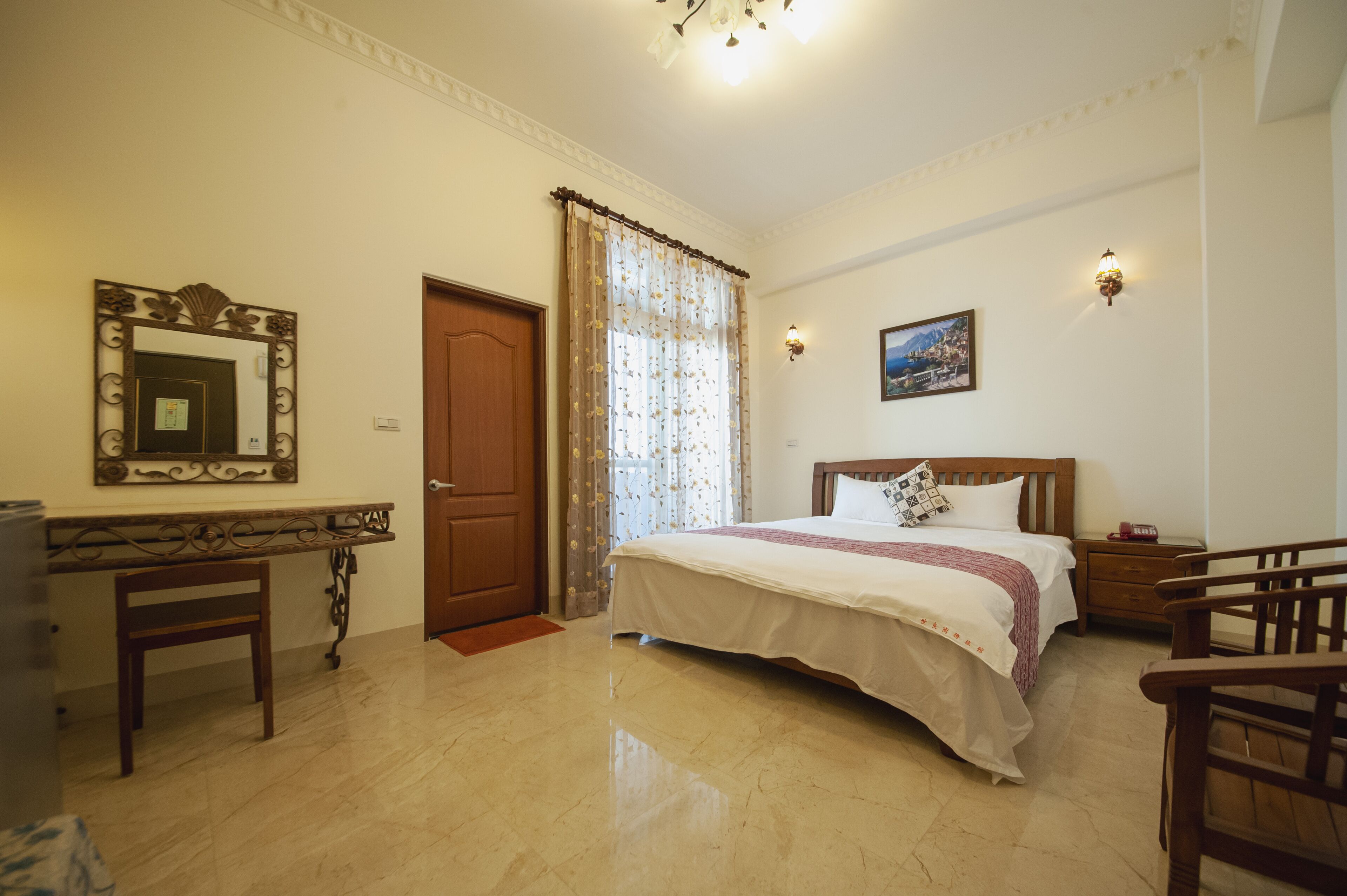 A hotel room with a bed, a desk, a chair, a wooden door, and a mirror.