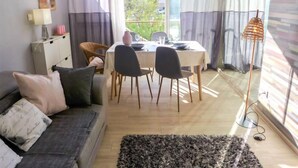 A cozy living room with a sofa, a dining table with chairs, a small cabinet, and a floor lamp.