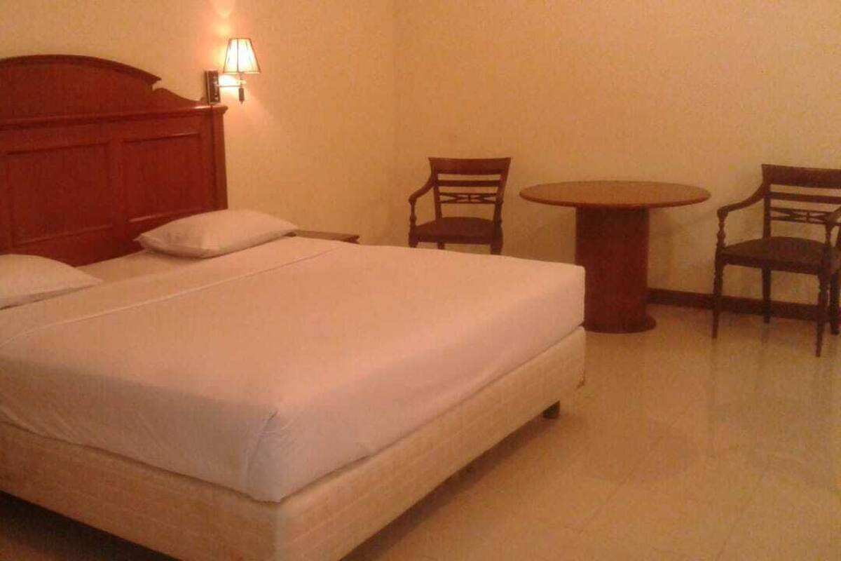 A hotel room with a large bed, two chairs, a small table, and a nightstand.