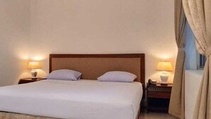Quarto de hotel com uma cama grande, duas mesas de cabeceira com luminárias e uma janela com cortinas.