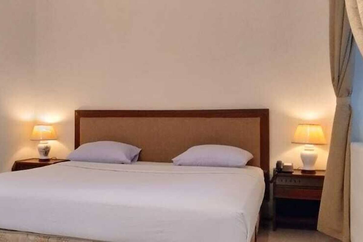 A hotel room with a large bed, two bedside tables with lamps, and a window with curtains.