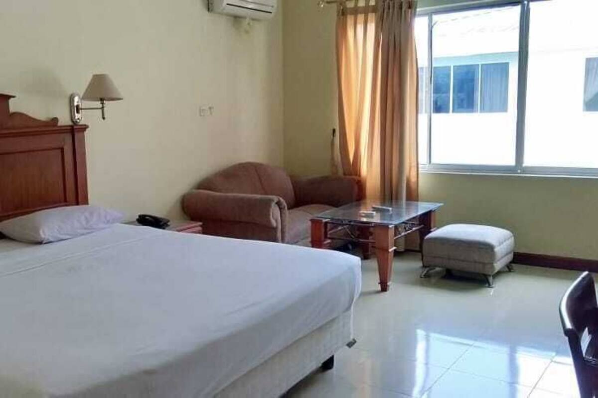 A hotel room with a large bed, a desk, a chair, and a window with curtains.