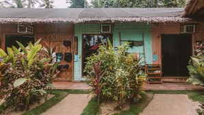 A rustic house with a thatched roof, a wooden door, and a small porch area with a bench.