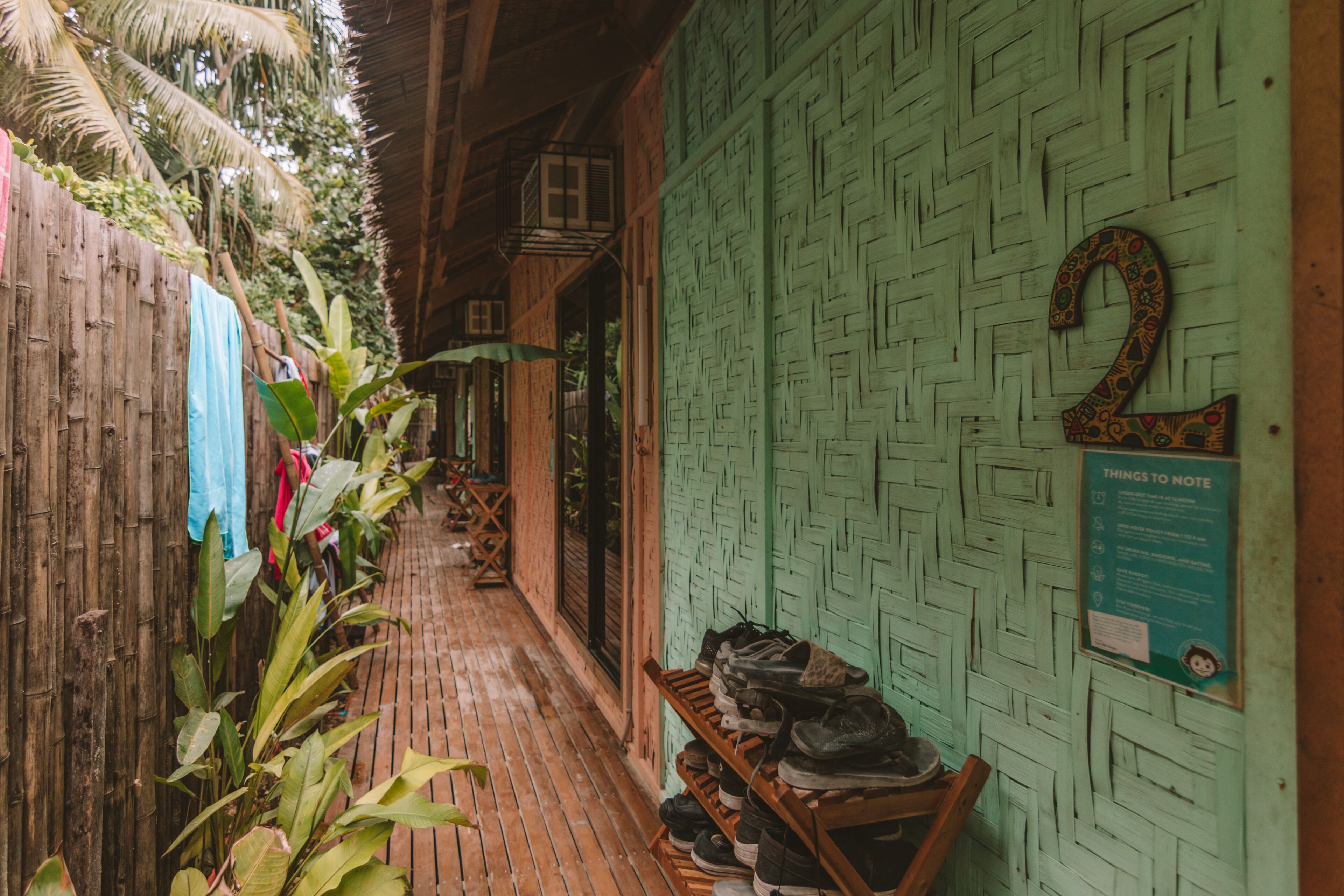 Un estrecho pasillo de madera con un muro tejido color verde y un zapatero de madera.