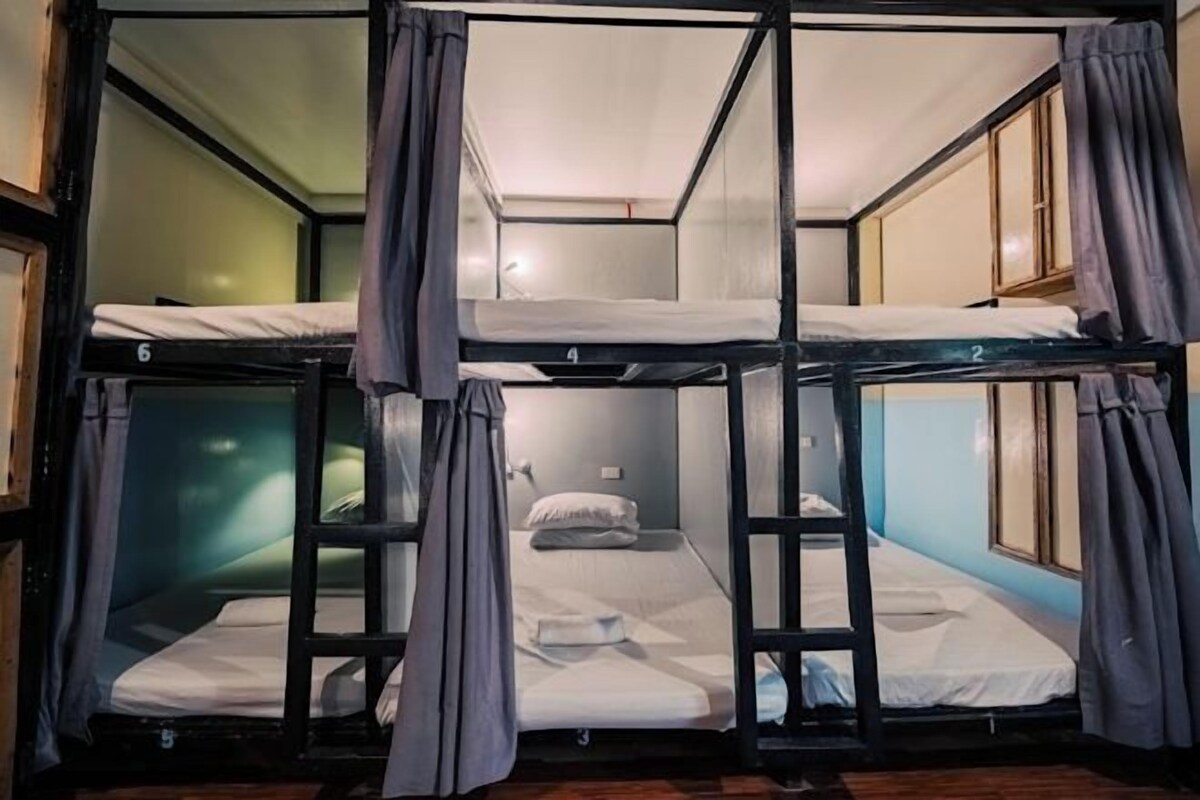 A bunk bed room with curtains, a window, and a wooden floor.