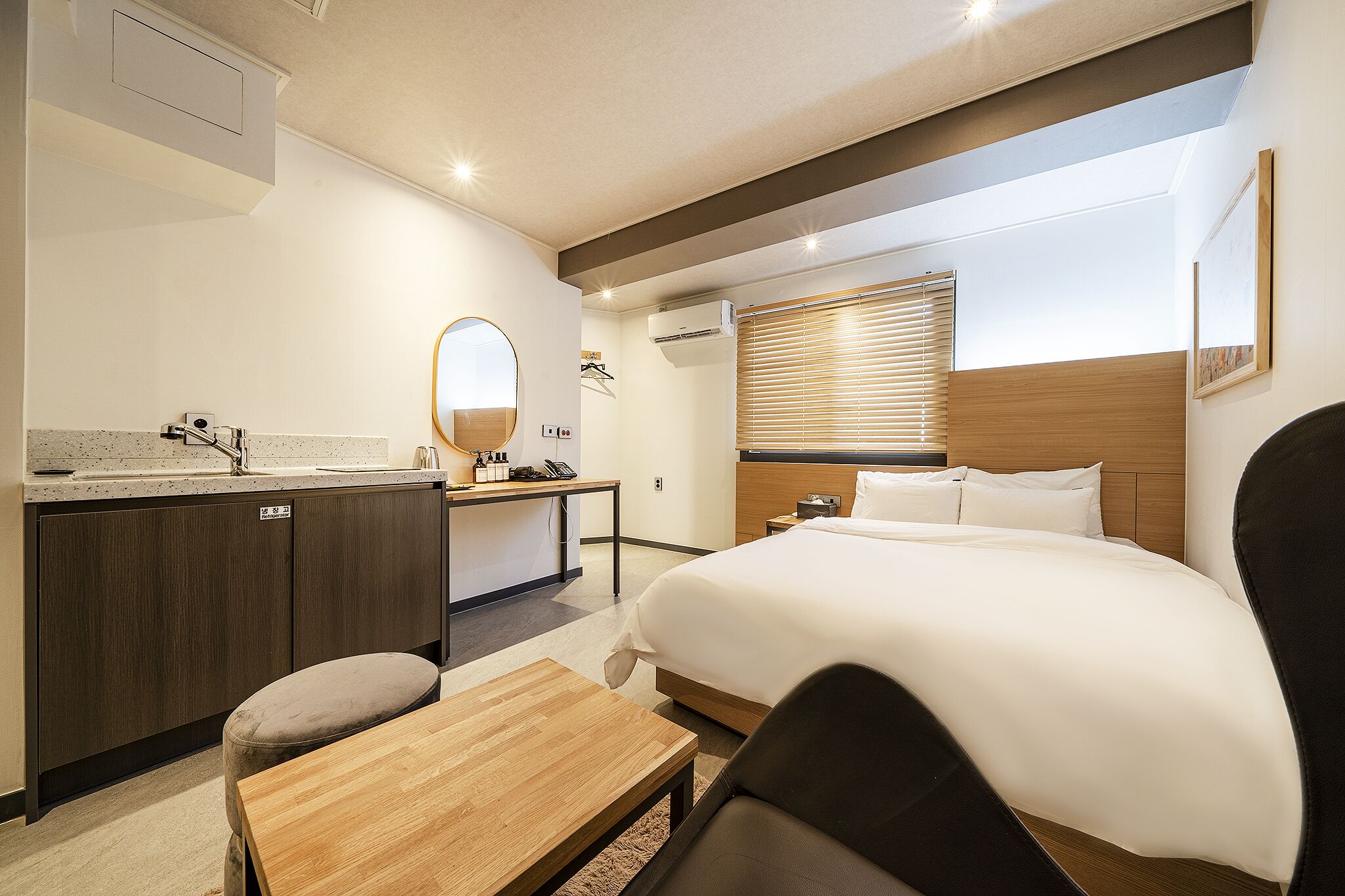 Habitación de hotel con cama, escritorio, silla, mesita, espejo y ventana con persianas.
