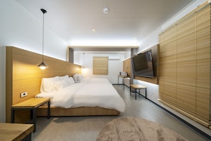 A modern bedroom with a large bed, bedside tables, a TV mounted on the wall, and a wooden headboard.