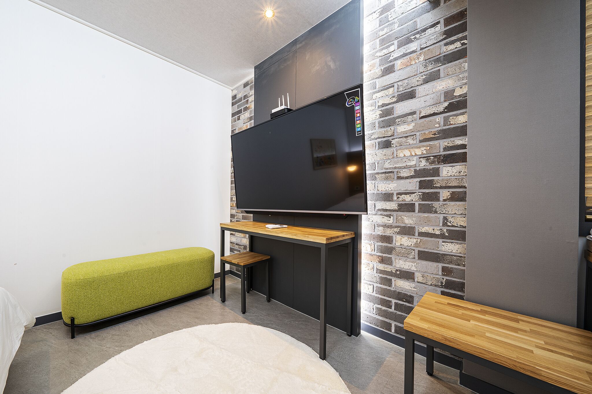 Un espace de vie moderne avec un téléviseur à écran plat fixé à un mur en briques, un banc en bois, un petit tabouret et un canapé.