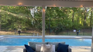 Un espacio al aire libre techado con piscina, zona de estar con cojines e iluminación con guirnaldas.