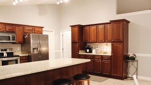 Una cocina con armarios de madera, electrodomésticos de acero inoxidable, una isla grande con taburetes y una zona de café.