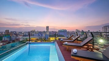 An infinity pool with lounge chairs and a city view at dusk.