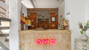 Un comptoir d’accueil avec une pancarte indiquant « Réception », une porte en bois ornée de sculptures complexes et un panneau néon qui épelle « OYO ».