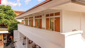 Un immeuble à plusieurs étages doté d’un balcon, de fenêtres avec des volets en bois et d’un arbre en arrière-plan.