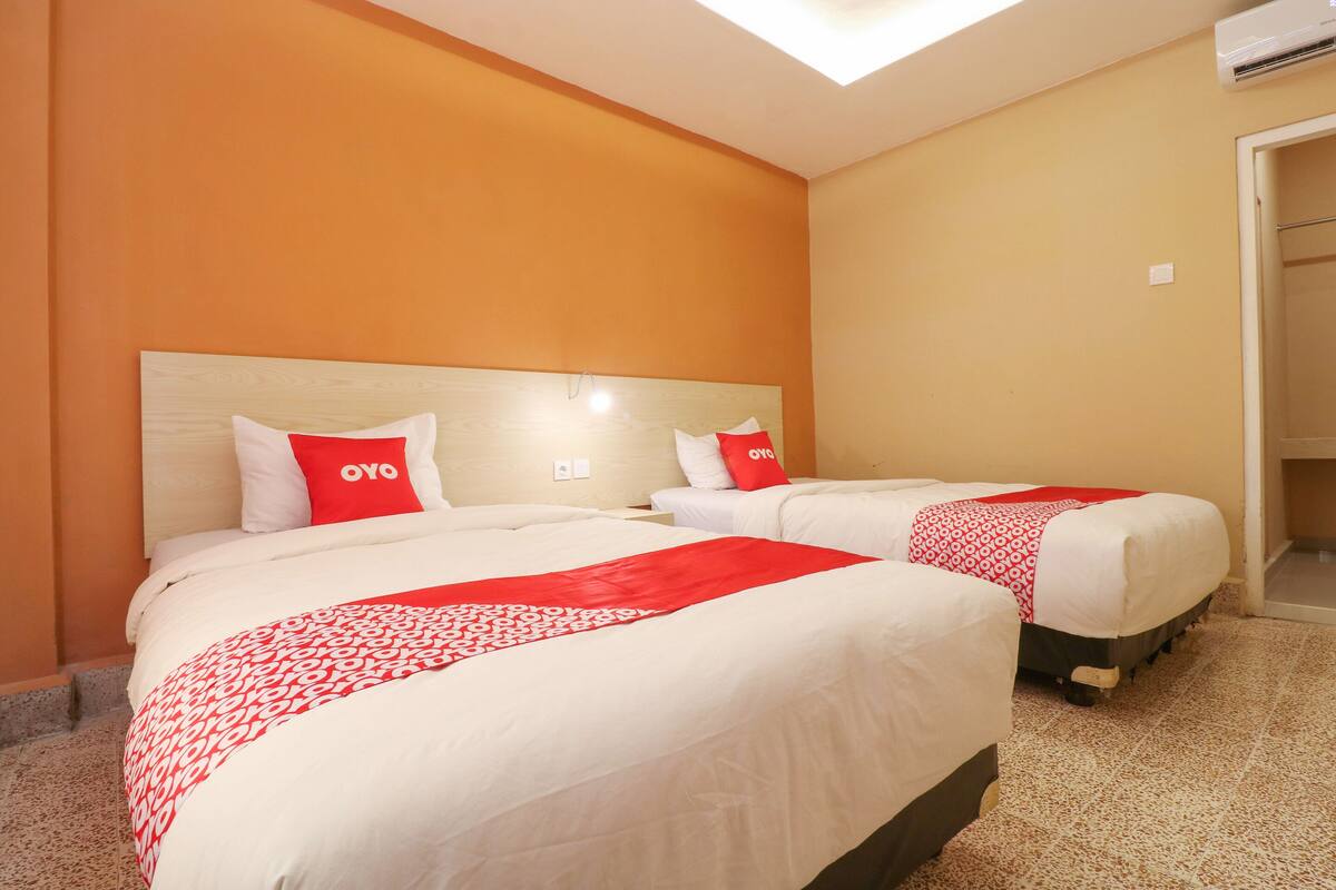 A hotel room with two beds, each with a red and white patterned bedspread and matching pillows.