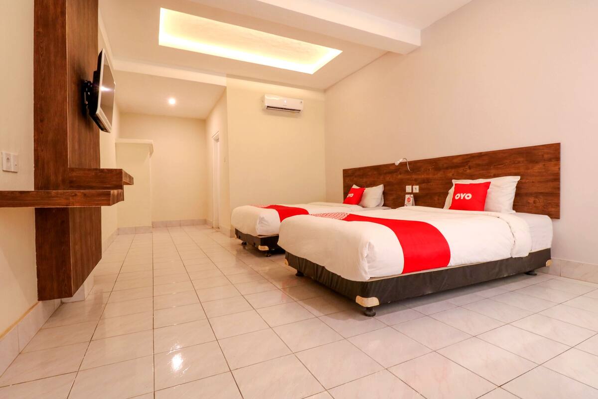 A hotel room with two beds, a wooden headboard, a flat-screen TV, and a ceiling light.