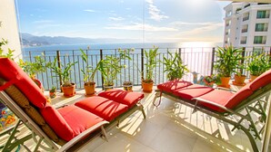 A balcony with red cushions, potted plants, and a view of the sea. - View and Breeze  w/cleaning service (Las Glorias)