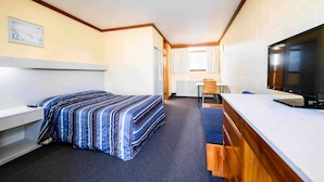 Una habitación de hotel pequeña con una cama individual, un escritorio, un televisor y una kitchenette.